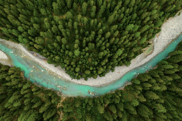 Inn River flowing in the forest in Switzerland. Aerial view from drone on a blue river in the mountains